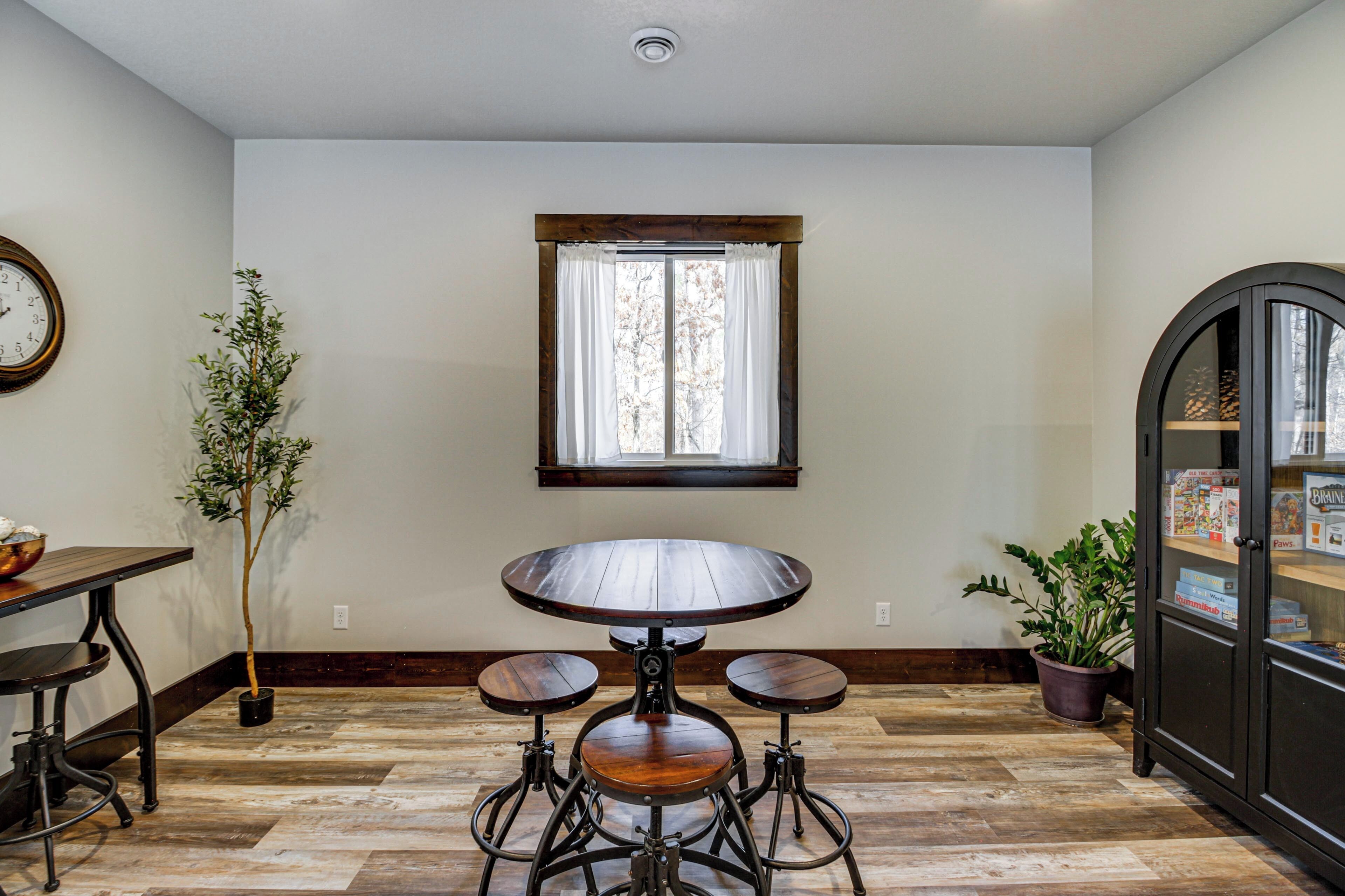 A dining area with a round table, two chairs, a potted plant, a clock, and a window with curtains.