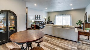 A living room with a wooden dining table, a sofa, a cabinet with glass doors, and a window with curtains. - 4 Mi to Golf: Family Home in Nisswa, Near Lakes! (Nisswa)