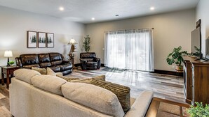 Un salon avec un canapé en cuir, un divan beige, un meuble en bois et une grande fenêtre ornée de rideaux légers.
