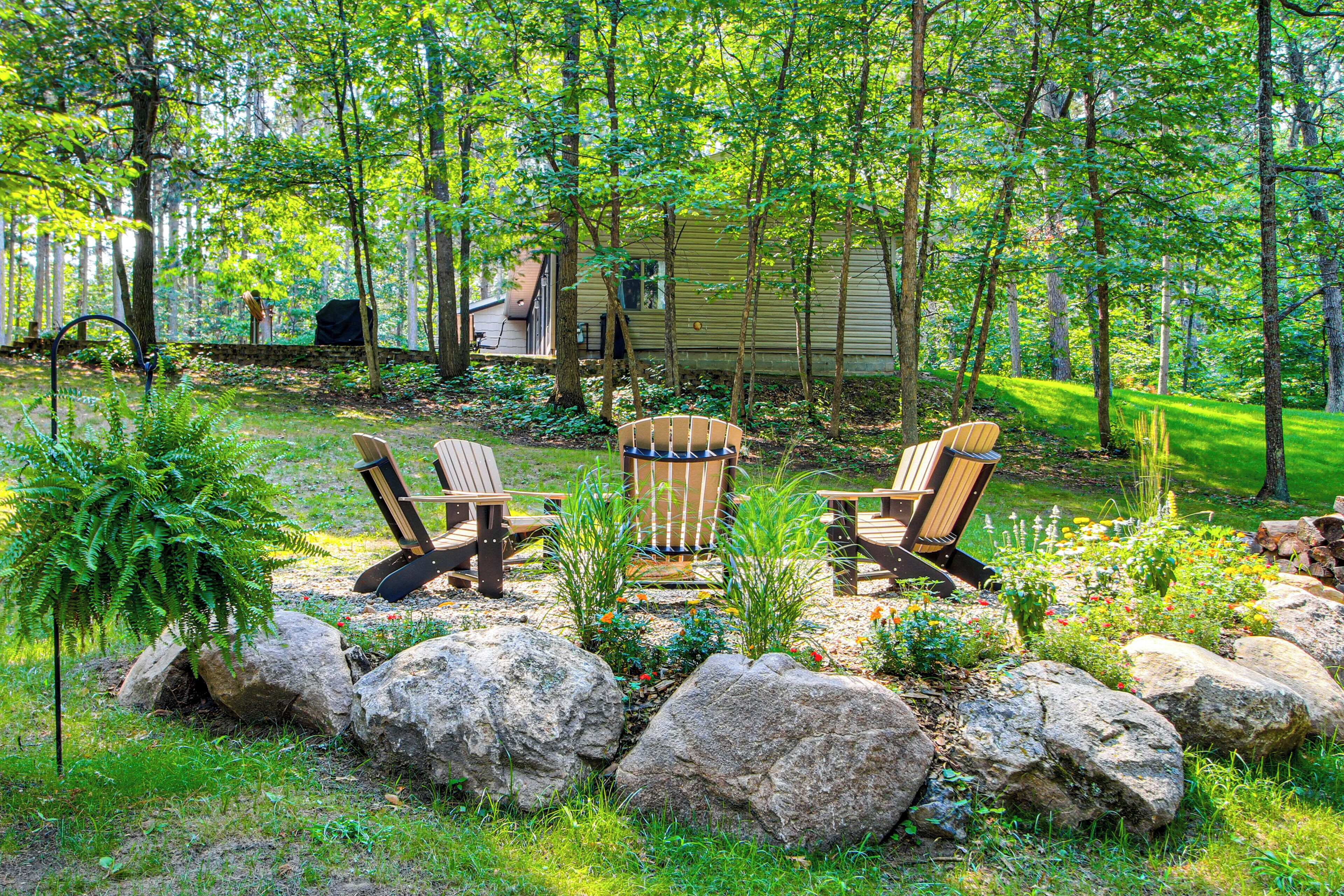 A wooden deck with Adirondack chairs, surrounded by large rocks and a garden with various plants.