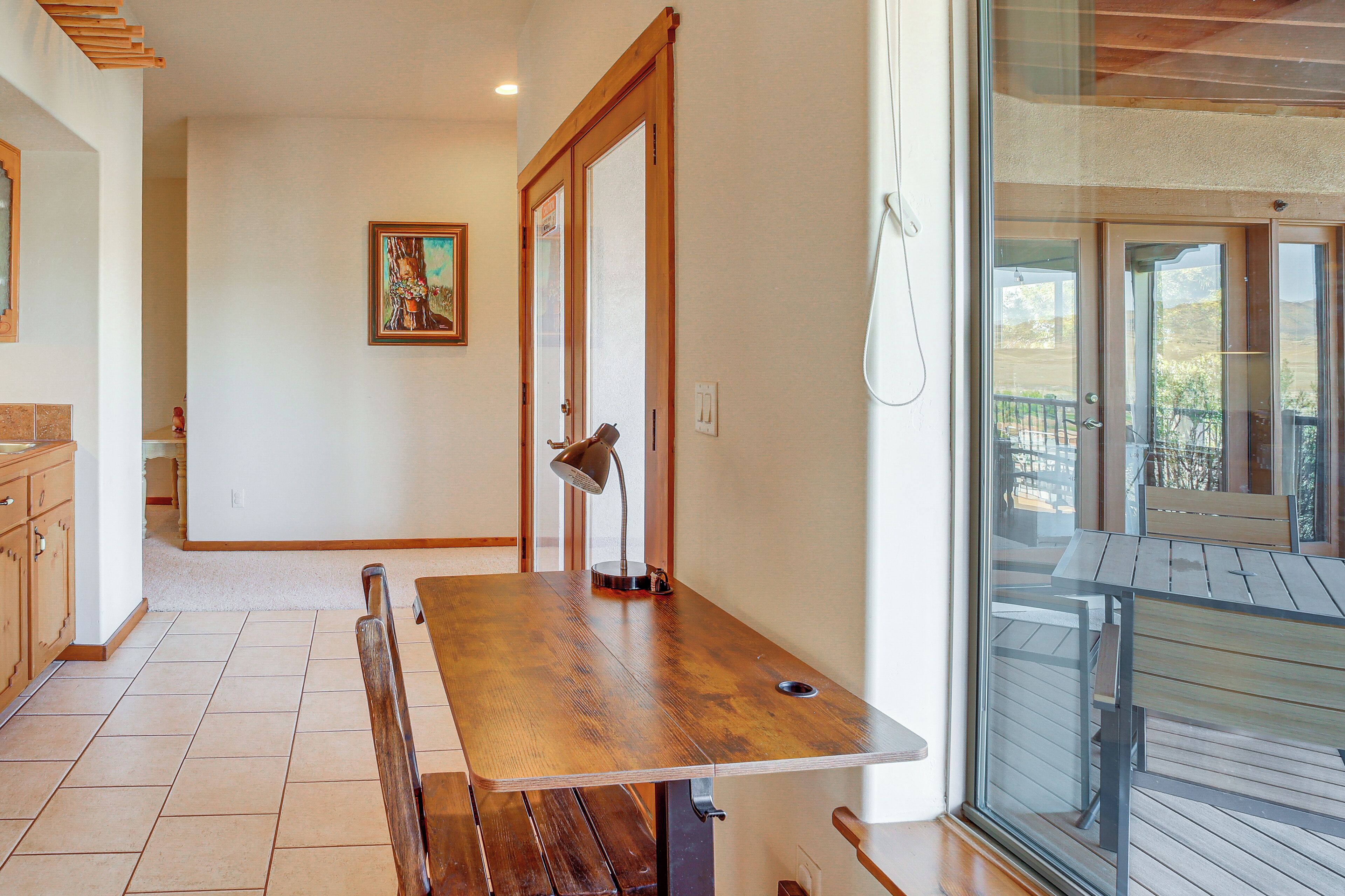A dining area with a wooden table and bench, a painting on the wall, and a view through a glass door.
