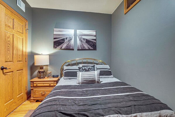 A bedroom with a bed, nightstand, lamp, and two wall-mounted pictures. - Sauna & Pool Table: Family Home on Lake Chicagon (Iron River)