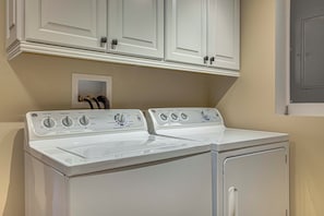 A front-loading washer and dryer in a laundry room with white cabinetry and a beige wall.