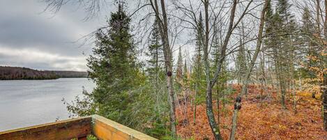 A wooden deck overlooking a lake with trees and a grassy area.