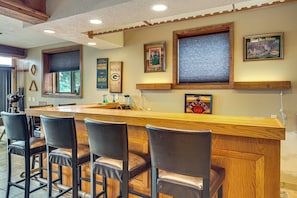A bar area with wooden counter and leather chairs, framed memorabilia on the wall, and a window with blinds.