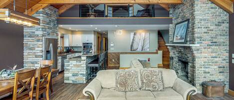 A spacious living area with a stone fireplace, wooden ceiling beams, and a dining area with a wooden table and chairs.