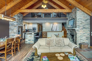 A spacious living area with a stone fireplace, wooden ceiling beams, and a dining area with a wooden table and chairs.