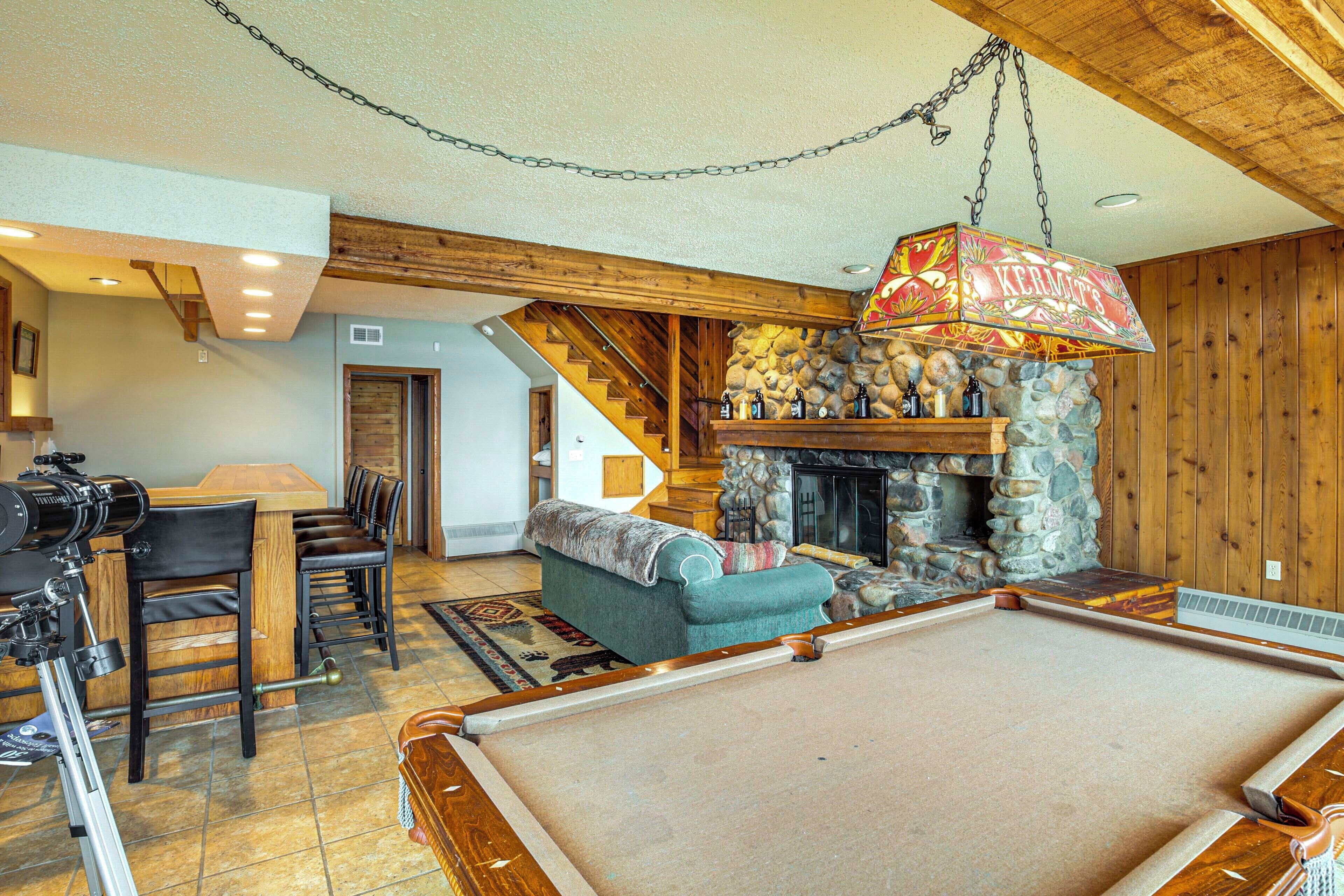 A cozy living room with a pool table, a fireplace, and a dining area with wooden chairs and a table.