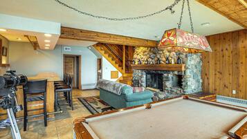 A cozy living room with a pool table, a fireplace, and a dining area with wooden chairs and a table.