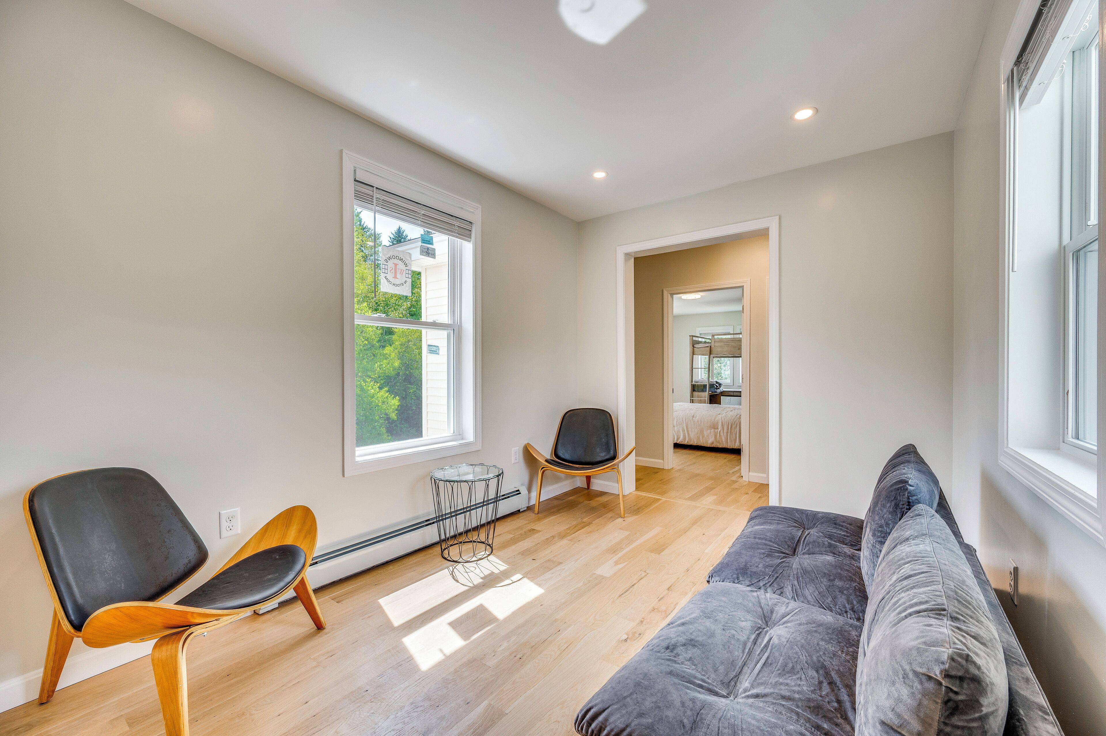 A modern living room with a grey sofa, two chairs, a radiator, and a window with blinds.