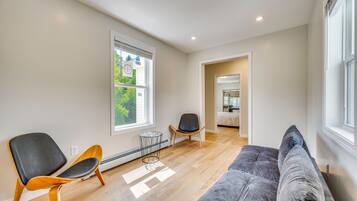 A modern living room with a grey sofa, two chairs, a radiator, and a window with blinds.