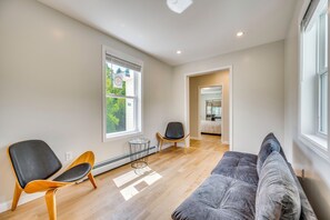 A modern living room with a grey sofa, two chairs, a radiator, and a window with blinds. - Explore the White Mountains! Spacious Rural Home (Thornton)
