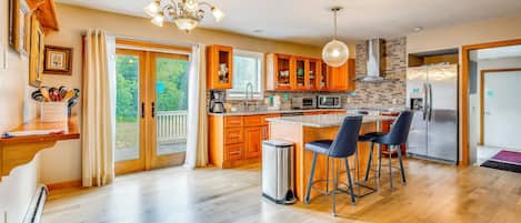 A modern kitchen with wooden cabinets, a stainless steel refrigerator, and a large island with bar stools.