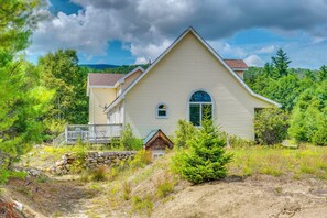 A two-story house with a gabled roof, a front porch, and a stone wall. - Explore the White Mountains! Spacious Rural Home (Thornton)