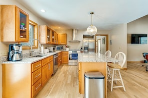 A modern kitchen with wooden cabinets, stainless steel appliances, a granite countertop, and a bar stool.