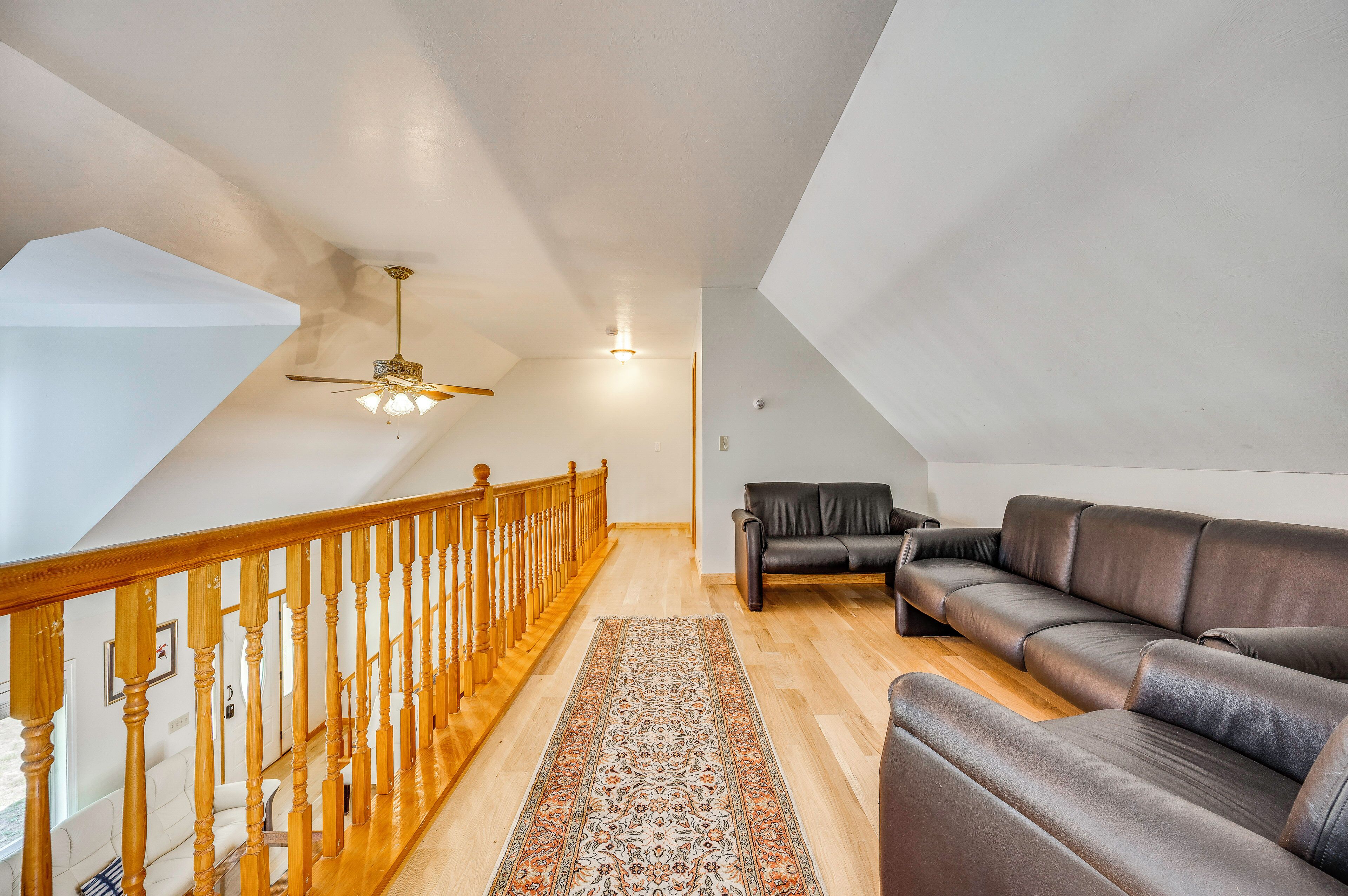 A spacious loft with a wooden staircase, a ceiling fan, a leather sofa, and a patterned rug.