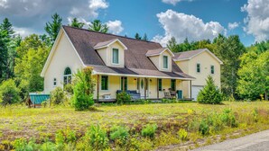 Ein zweistöckiges Haus mit Veranda, umgeben von einem Feld und Bäumen.
