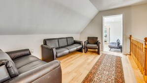 A loft-style living room with a high ceiling, a wooden floor, and a view through an open door to a bedroom. - Explore the White Mountains! Spacious Rural Home (Thornton)