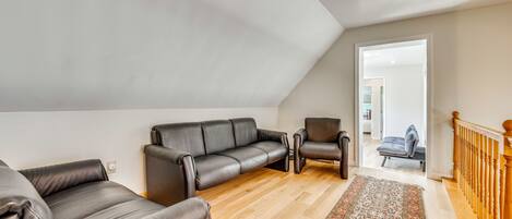 A loft-style living room with a high ceiling, a wooden floor, and a view through an open door to a bedroom.