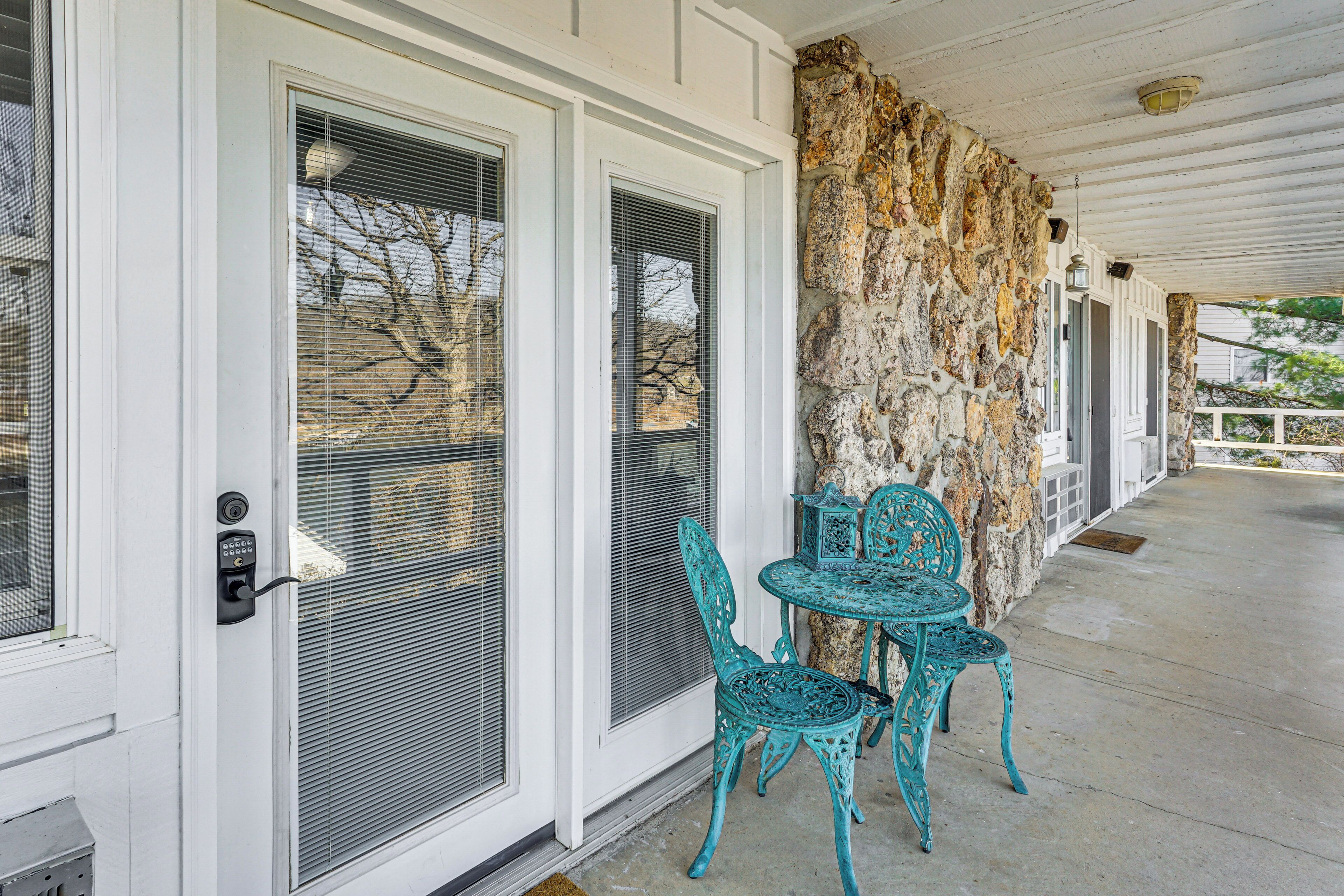 A covered porch with a stone wall, a door with a security keypad, and turquoise metal chairs.