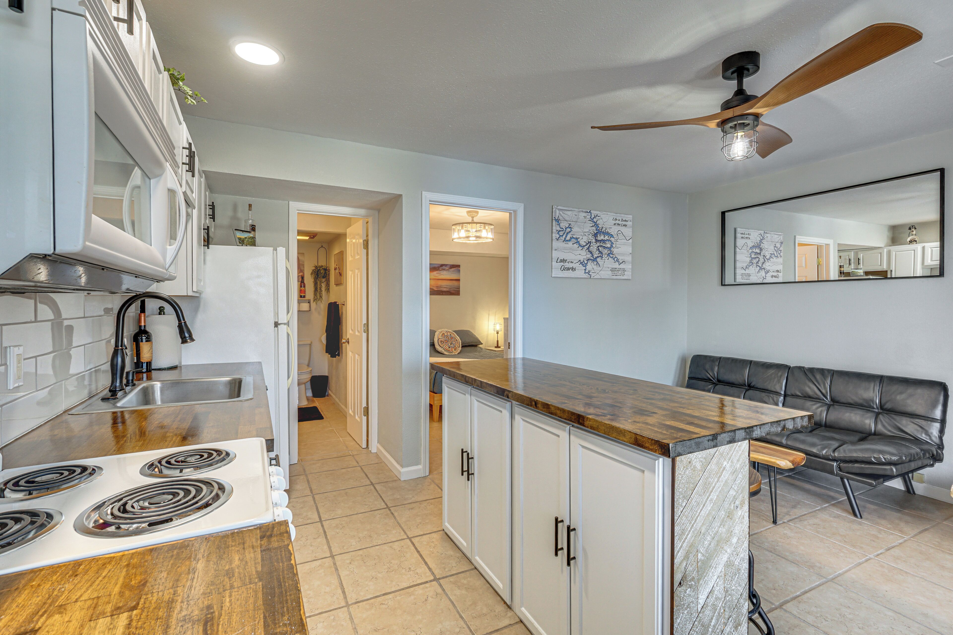A kitchen with a stove, cabinets, a countertop, a ceiling fan, and a dining area with a sofa.