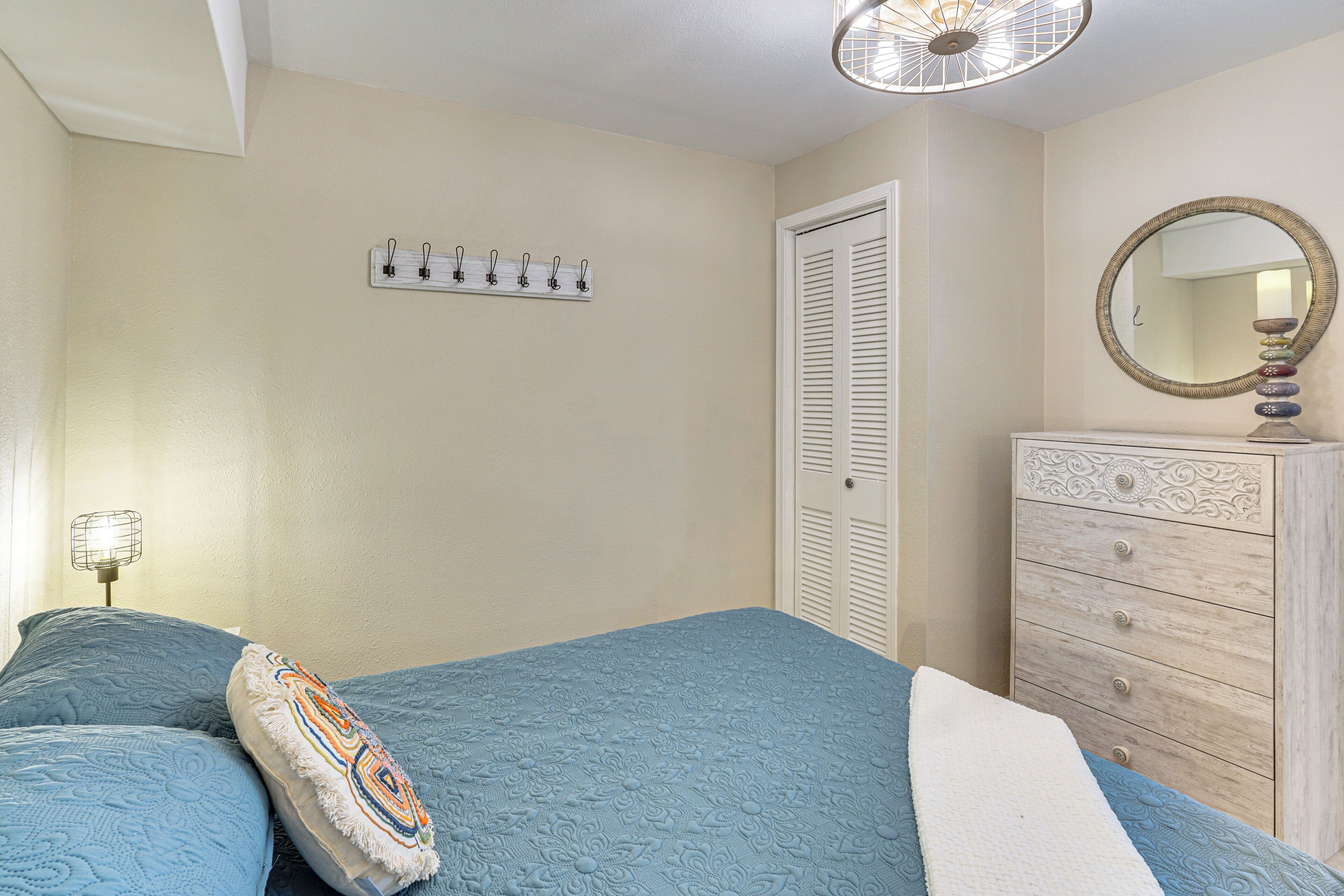A bedroom with a bed, dresser, mirror, and wall-mounted hooks.