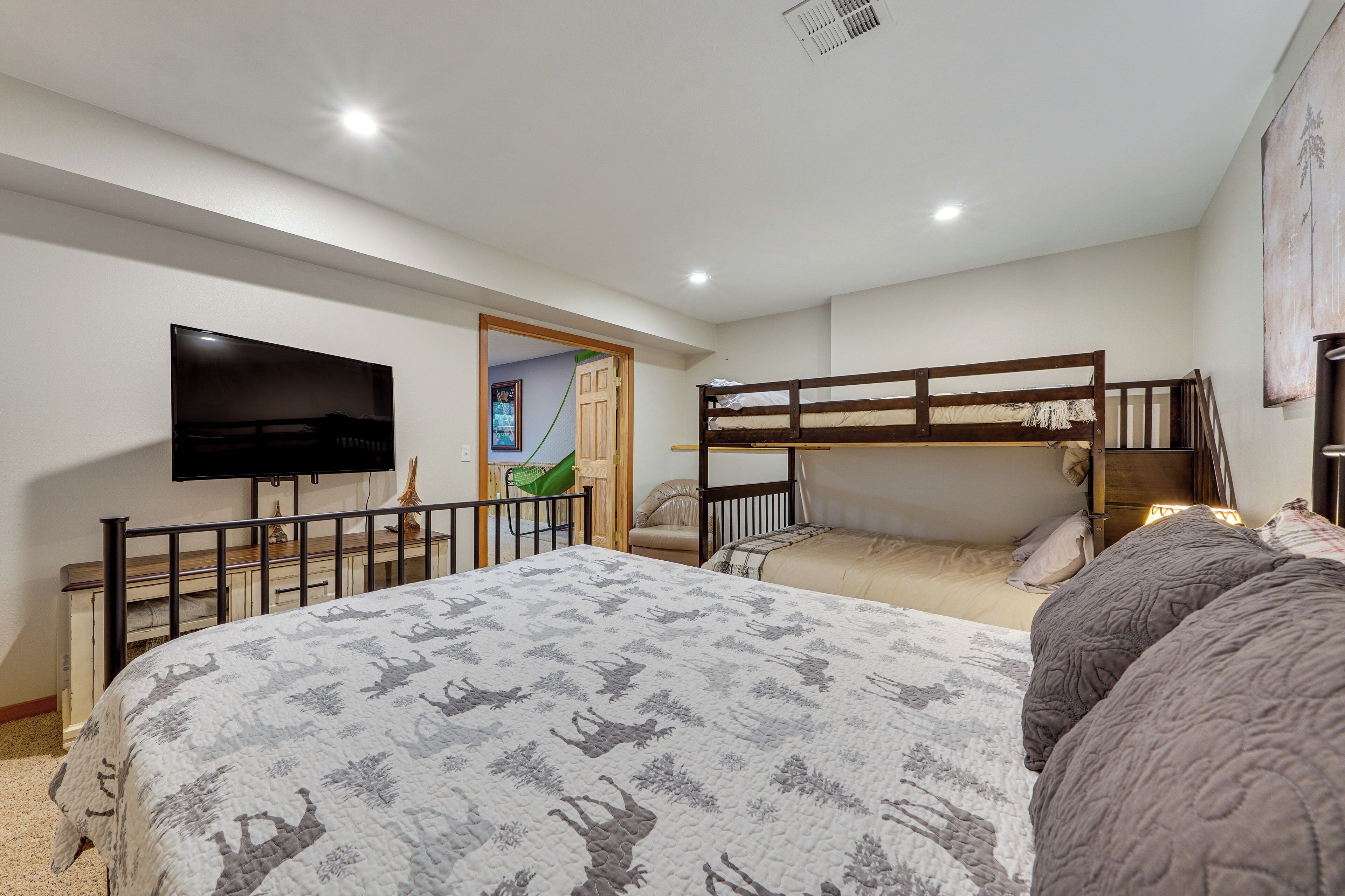 A bedroom with a large bed, a TV, bunk beds, and a door leading to another room.