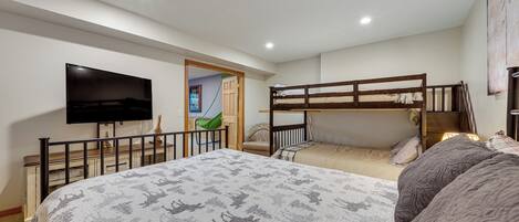 A bedroom with a large bed, a TV, bunk beds, and a door leading to another room.