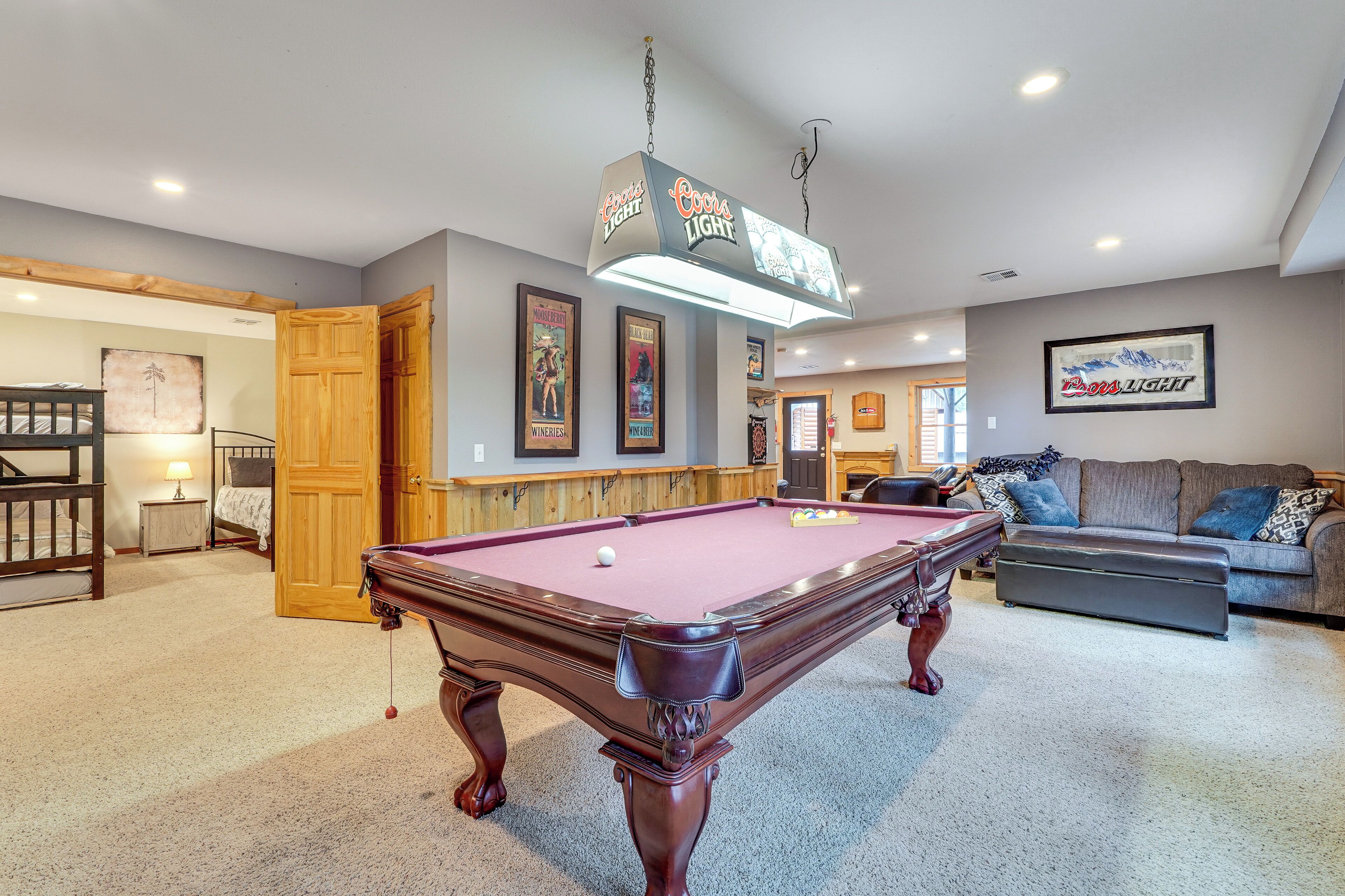 A pool table in a room with a bar area, a sofa, and framed pictures on the wall.