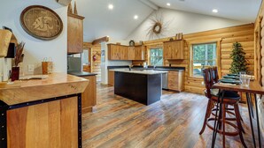 Cucina in stile baita con mobili in legno, un'isola centrale e una zona pranzo con sedie.