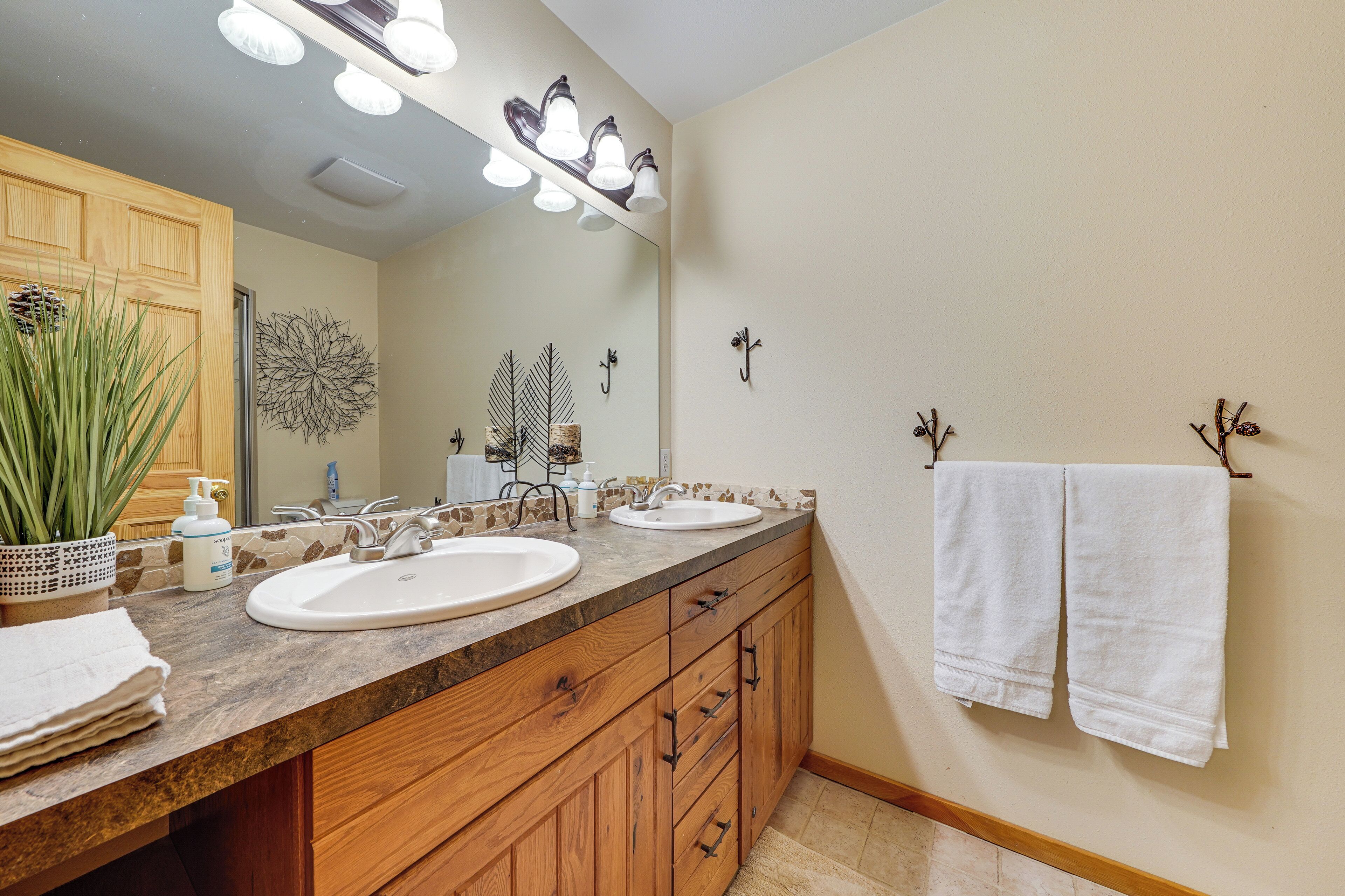 A bathroom with two sinks, wooden cabinets, a large mirror, and decorative wall hooks.