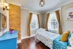 Quarto com parede de tijolos, cabeceira branca, penteadeira azul e cama com roupa de cama floral.