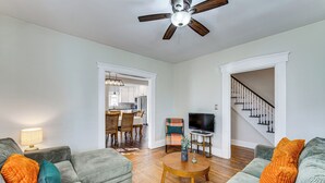 Un salon avec un ventilateur de plafond, un coin repas avec des chaises, un téléviseur et un escalier.