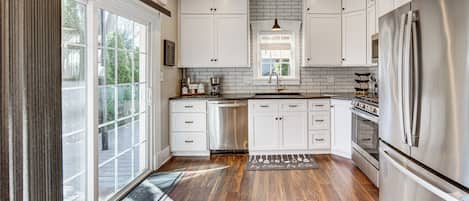 A kitchen with white cabinets, a stainless steel refrigerator, and a large window.