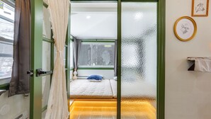 Ein Schlafzimmer mit einer Schiebeglastür, einem Bett mit blauem Kopfkissen, einem kleinen Fenster und einem an der Wand befestigten Handtuchhalter.