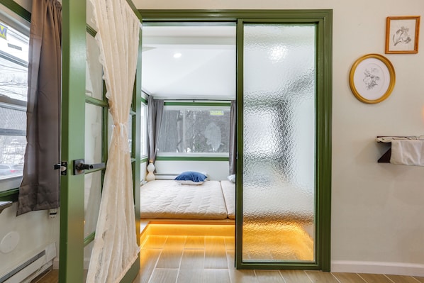 A bedroom with a sliding glass door, a bed with a blue pillow, a small window, and a wall-mounted towel rack. - Lakeside Charm! Updated Home Near Mtn Creek Resort (West Milford)