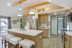 A modern kitchen with a central island, wooden stools, stainless steel appliances, and a staircase with a wooden railing. - Lakeside Charm! Updated Home Near Mtn Creek Resort (West Milford)