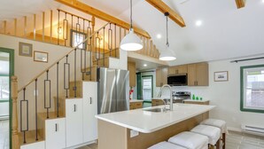 Eine moderne Küche mit einer zentralen Kochinsel, Edelstahlgeräten, einer Holztreppe und Pendelleuchten.