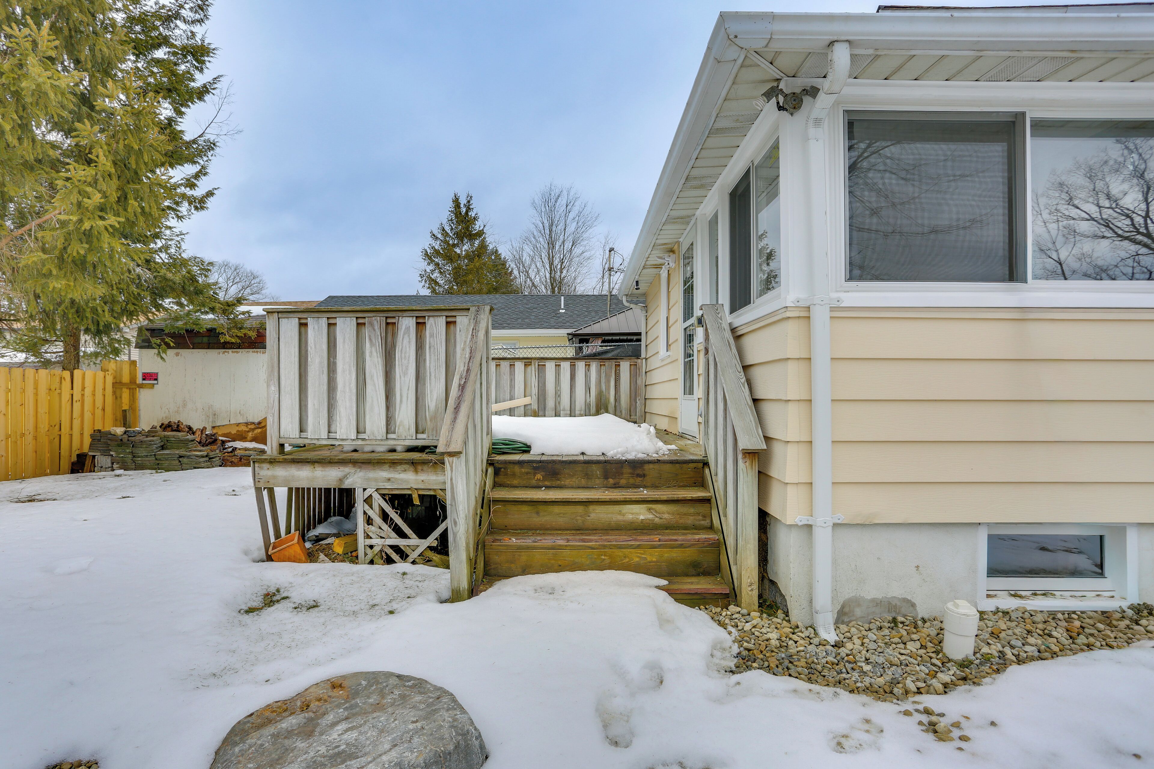 A house with a wooden deck, a set of stairs leading to the front door, and a snow-covered yard.