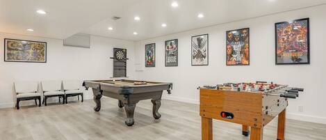 Une pièce équipée d’une table de billard, d’un baby-foot et de plusieurs affiches encadrées accrochées au mur.