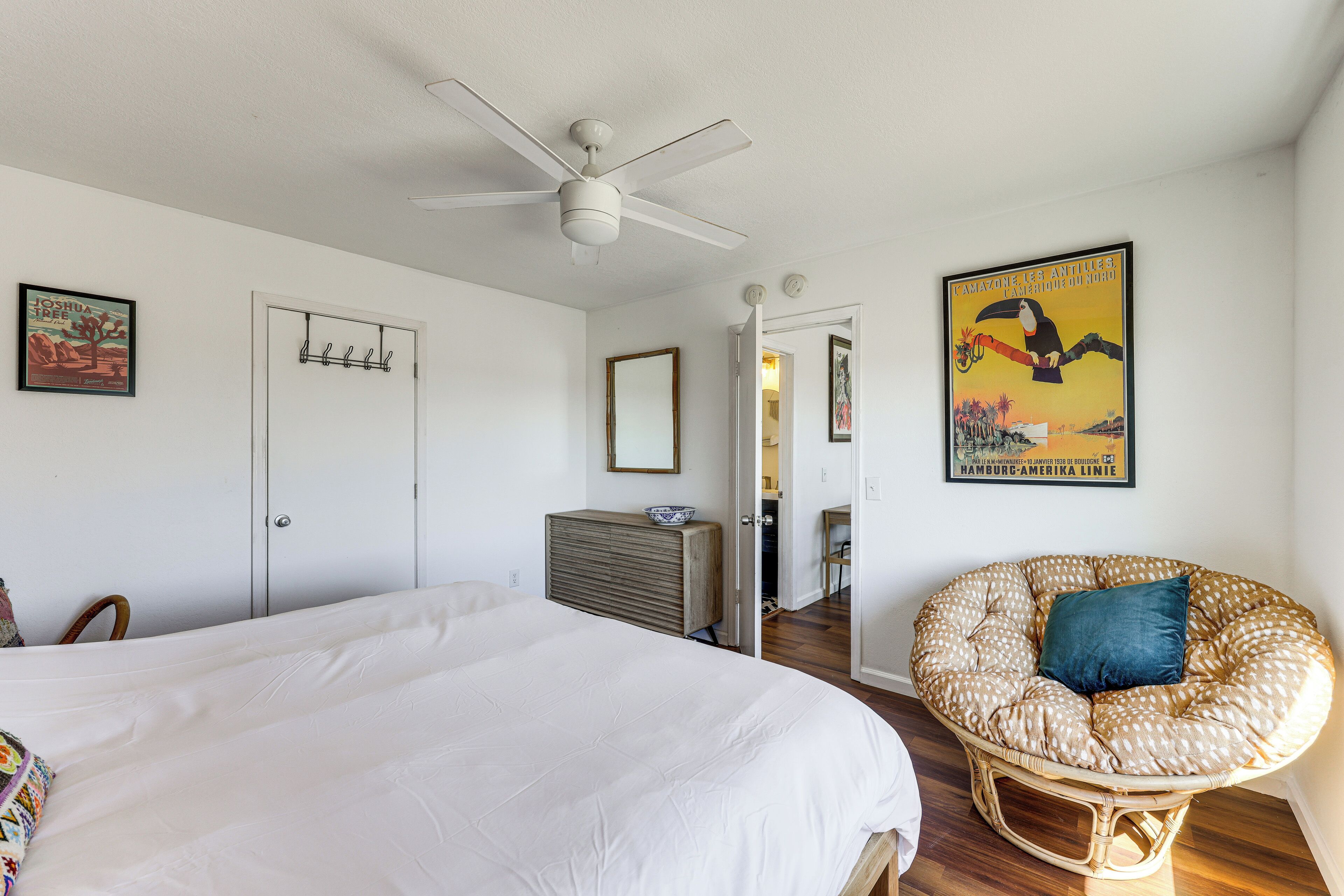 A bedroom with a bed, a ceiling fan, a chair, a door, and a poster on the wall.