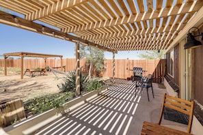 Un espacio de patio cubierto con un pérgola de madera, mobiliario exterior y una parrilla de barbacoa.