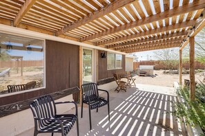 Eine überdachte Terrasse mit Holzbalken, zwei Stühlen, einem Tisch und Blick auf einen eingezäunten Außenbereich.