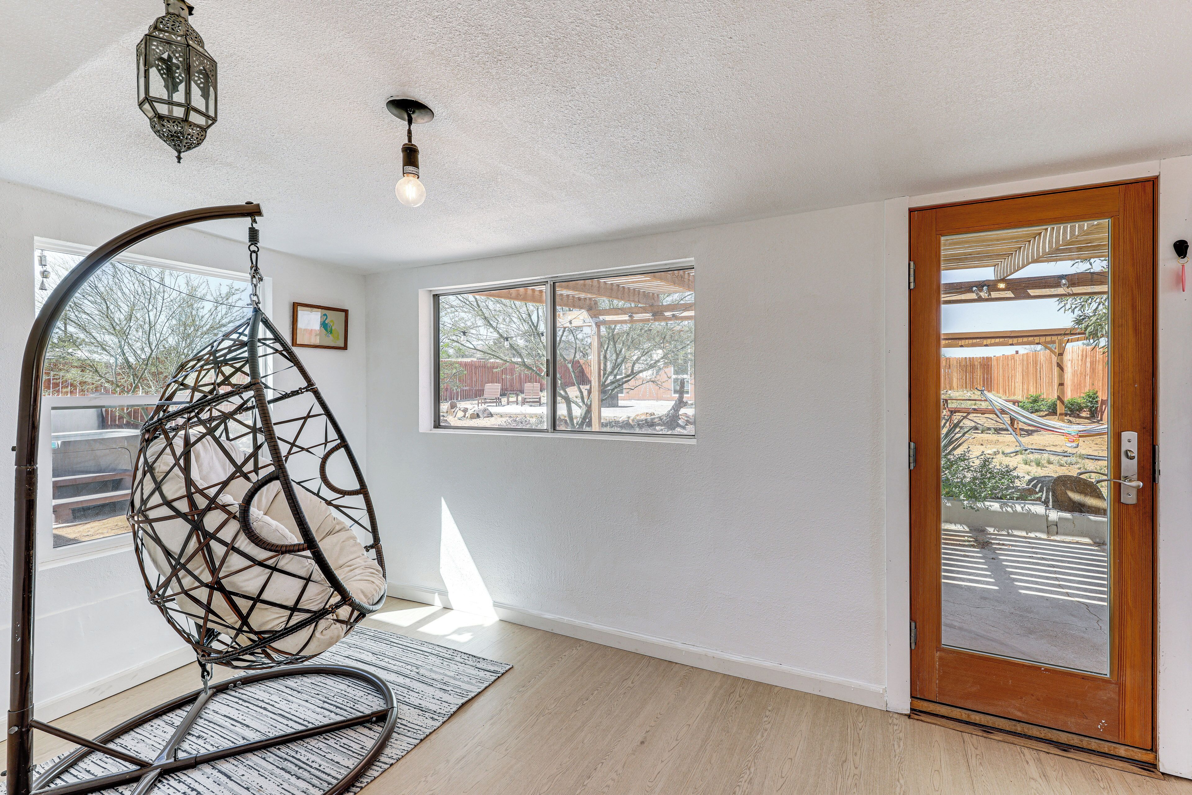 Una habitación con una silla colgante, una puerta de madera y un ventanal grande.