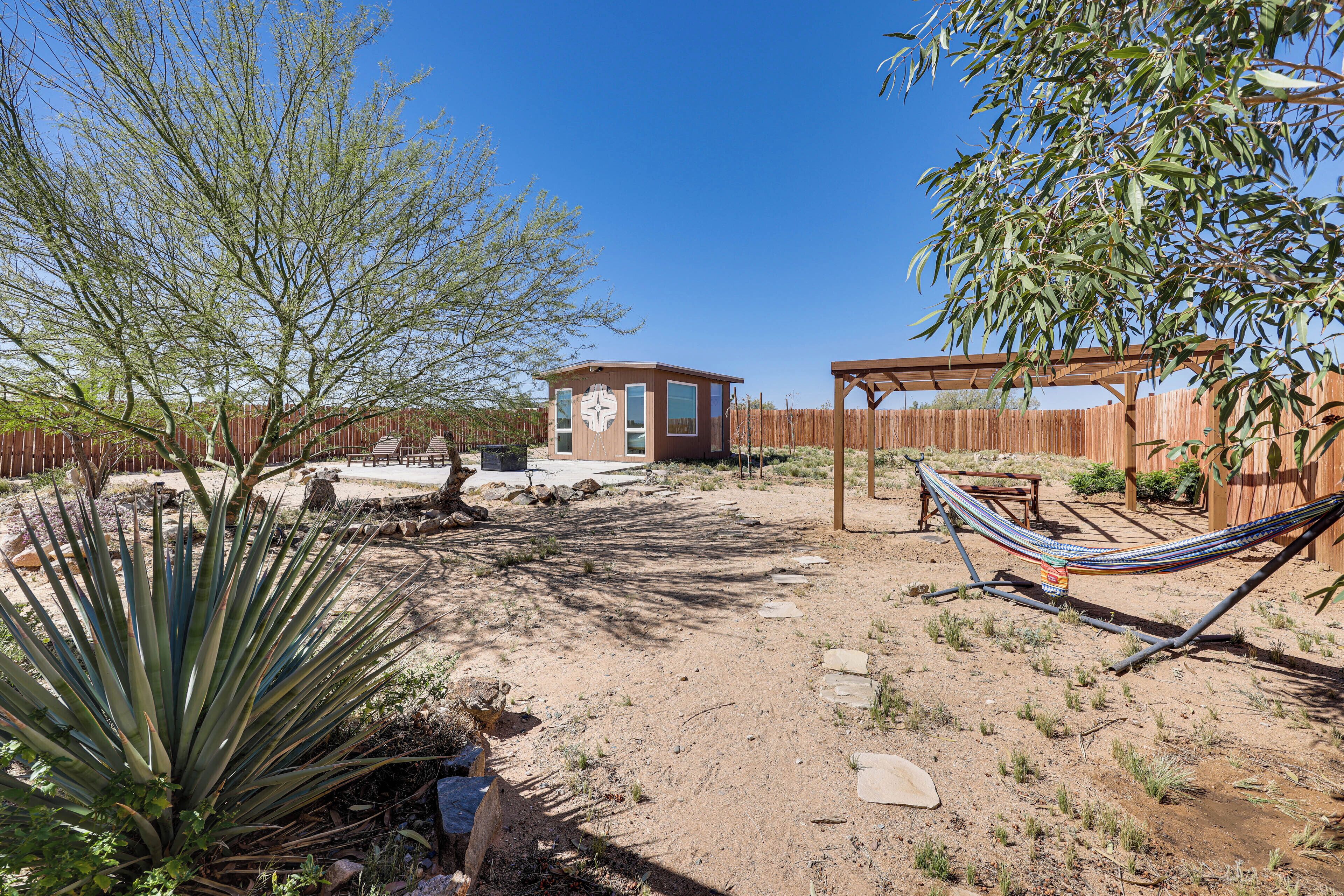 A fenced backyard with a small wooden structure, a hammock, and a large agave plant.