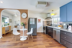 A modern kitchen with wooden flooring, white chairs, a dining table, and blue cabinets.