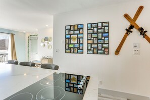 A modern hotel room with a large dining table, a ski rack, and a wall decorated with framed photos.