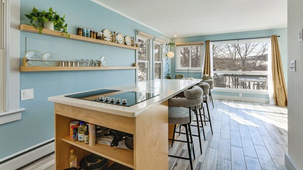 A modern kitchen with a central island, bar stools, and a view to an outdoor patio. - Lakefront Living By Mtn Creek! Modern Home w/ Deck (Sussex)