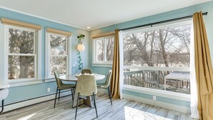 A dining area with a round table and chairs, large windows with curtains, and a view of outdoor furniture. - Lakefront Living By Mtn Creek! Modern Home w/ Deck (Sussex)