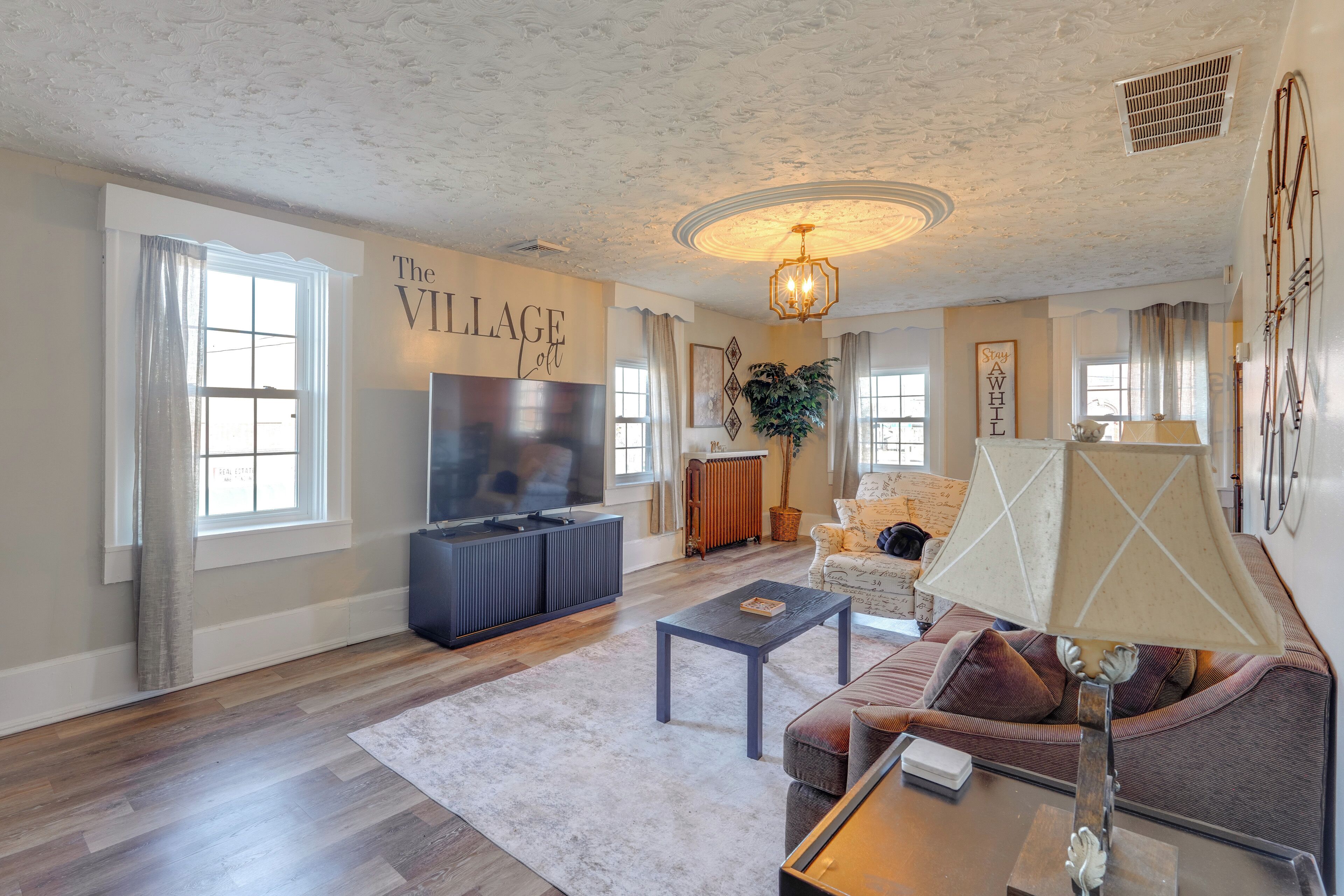 A living room with a TV, sofa, coffee table, and a sign that reads 'The Village Loft'.